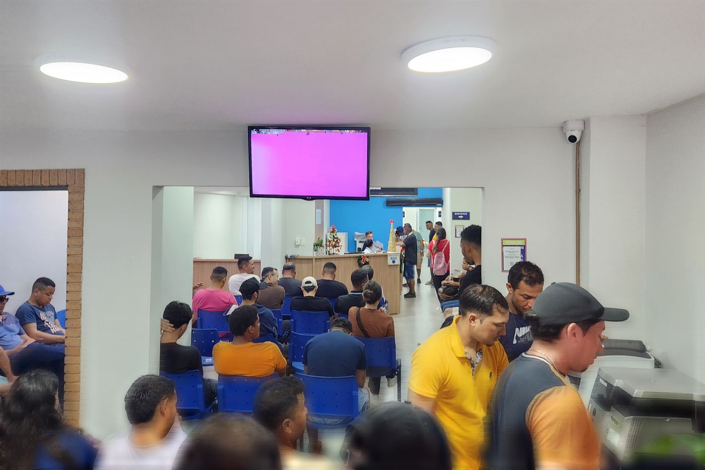 Balcão de atendimento da clínica, com o painel de senhas e a área de espera.
