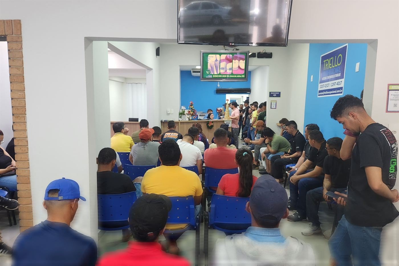 Sala de espera da clínica cheia em uma manhã de atendimento, com o painel da Triello ao fundo.